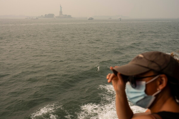 A person wearing a mask takes the Staten Island Ferry as smoke from wildfires blankets the sky, Thursday, July 16, 2026, in New York. (AP Photo/Yuki Iwamura)