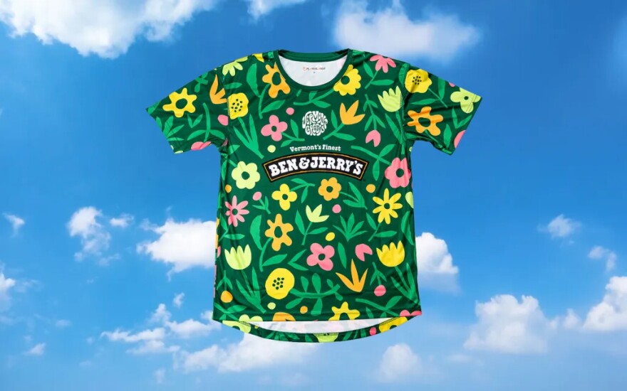 Green soccer training top with pink, orange and yellow flower designs and a Ben & Jerry's logo on a blue sky background.