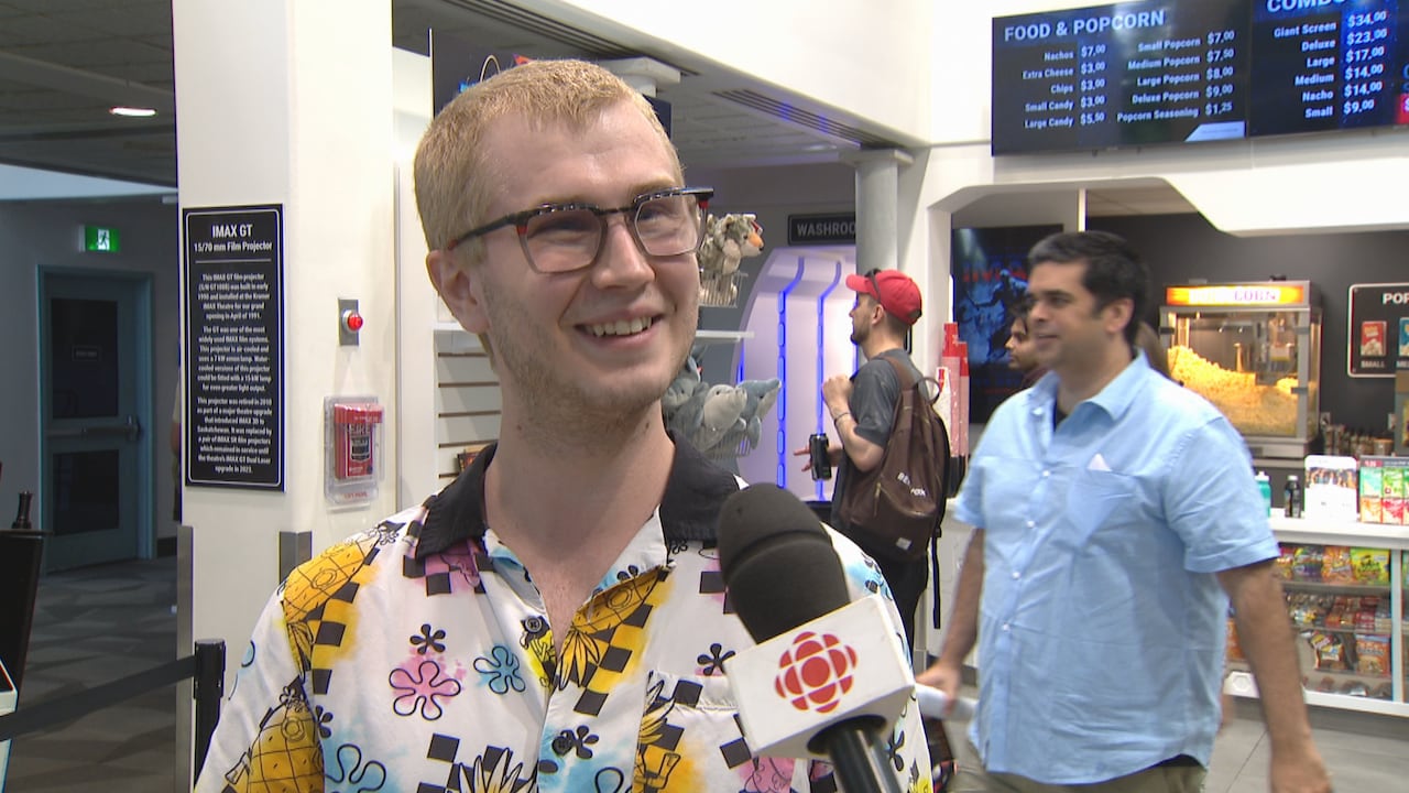 Man wearing glasses and a floral shirt smiling in a movie theatre lobby.