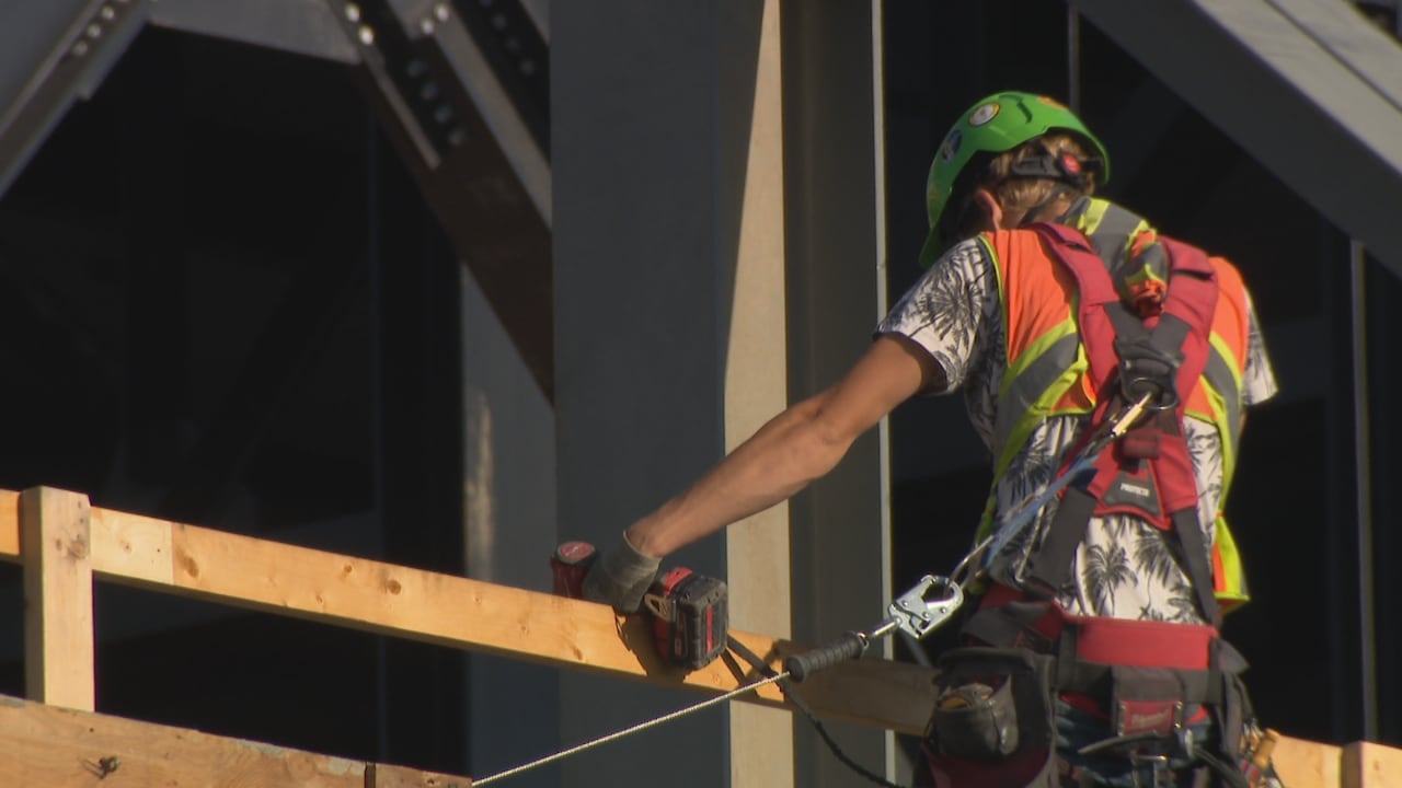 A close-up shot of the back of a construction worker holding a drill while wearing a high-visibility vest.