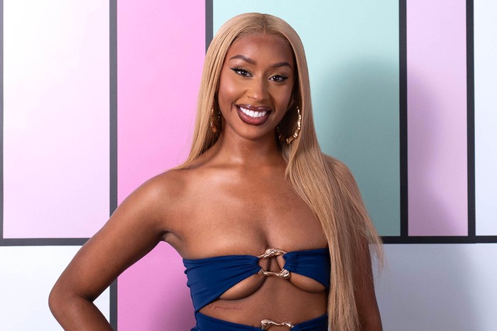 Love Island S13 Mara wearing a blue cut out swimsuit smiling ahead with one hand on her hip.