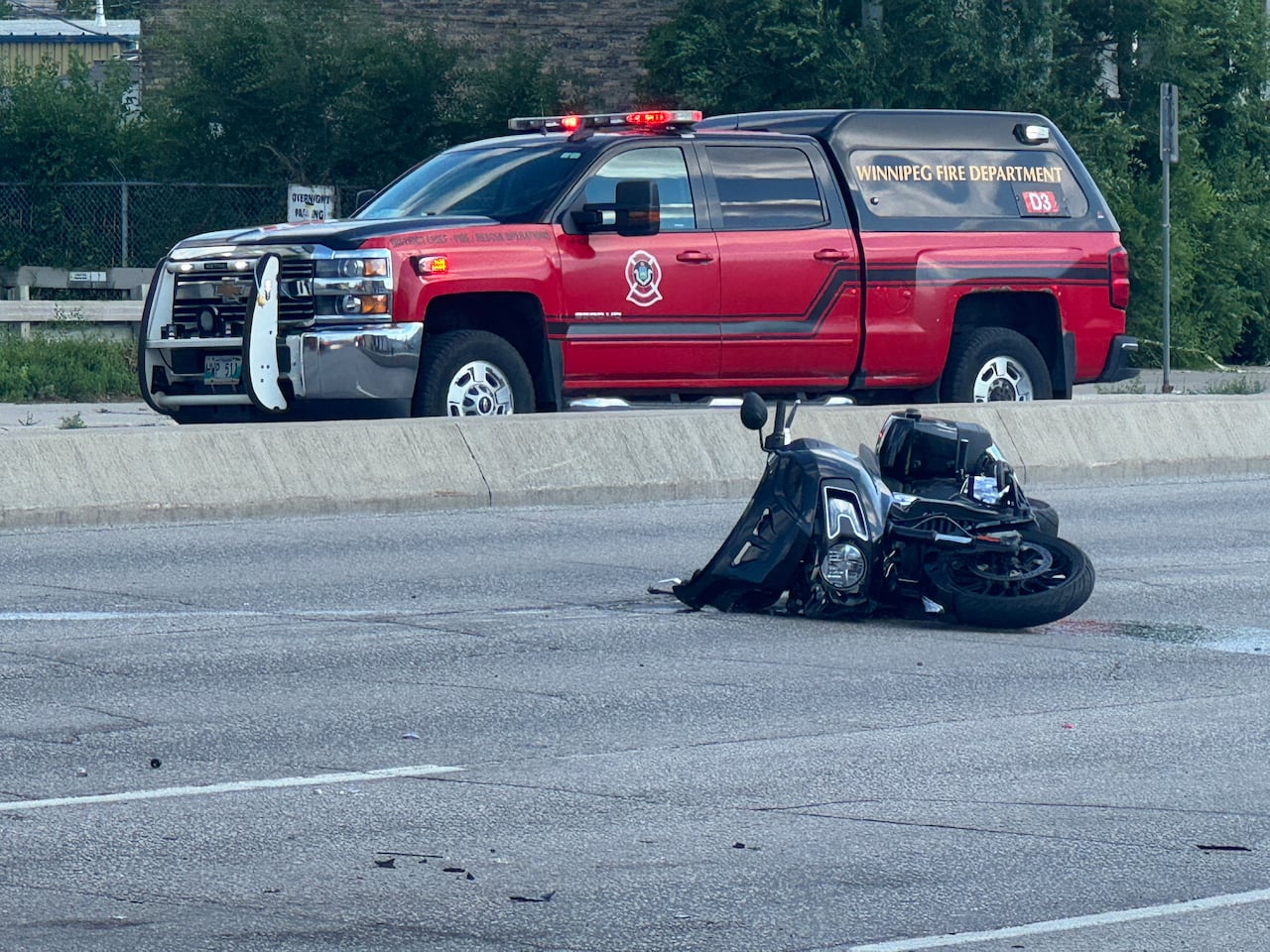 A motorcycle lays crumpled on the road with a fire department vehicle behind it