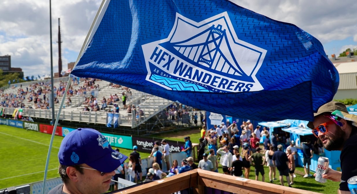A blue and white flag waves in the air at a soccer game. It reads, "HFX WANDERERS."