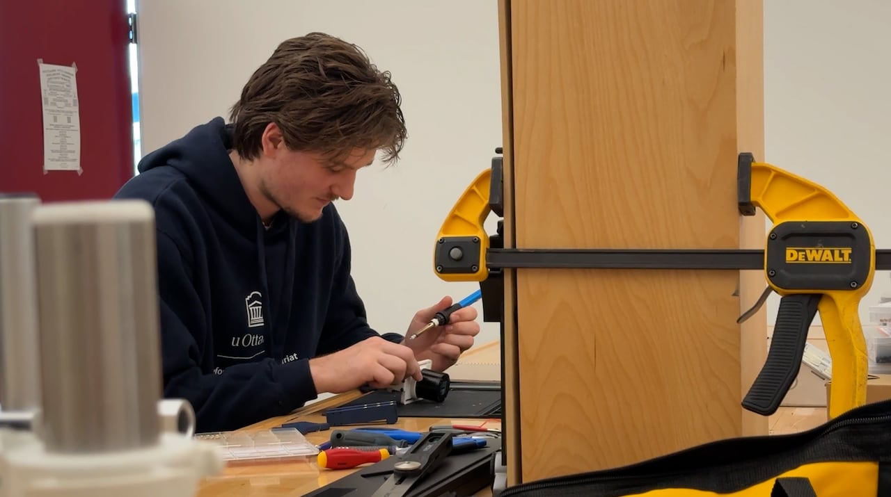 A man in a dark hooded sweatshirt uses a tool in a laboratory.