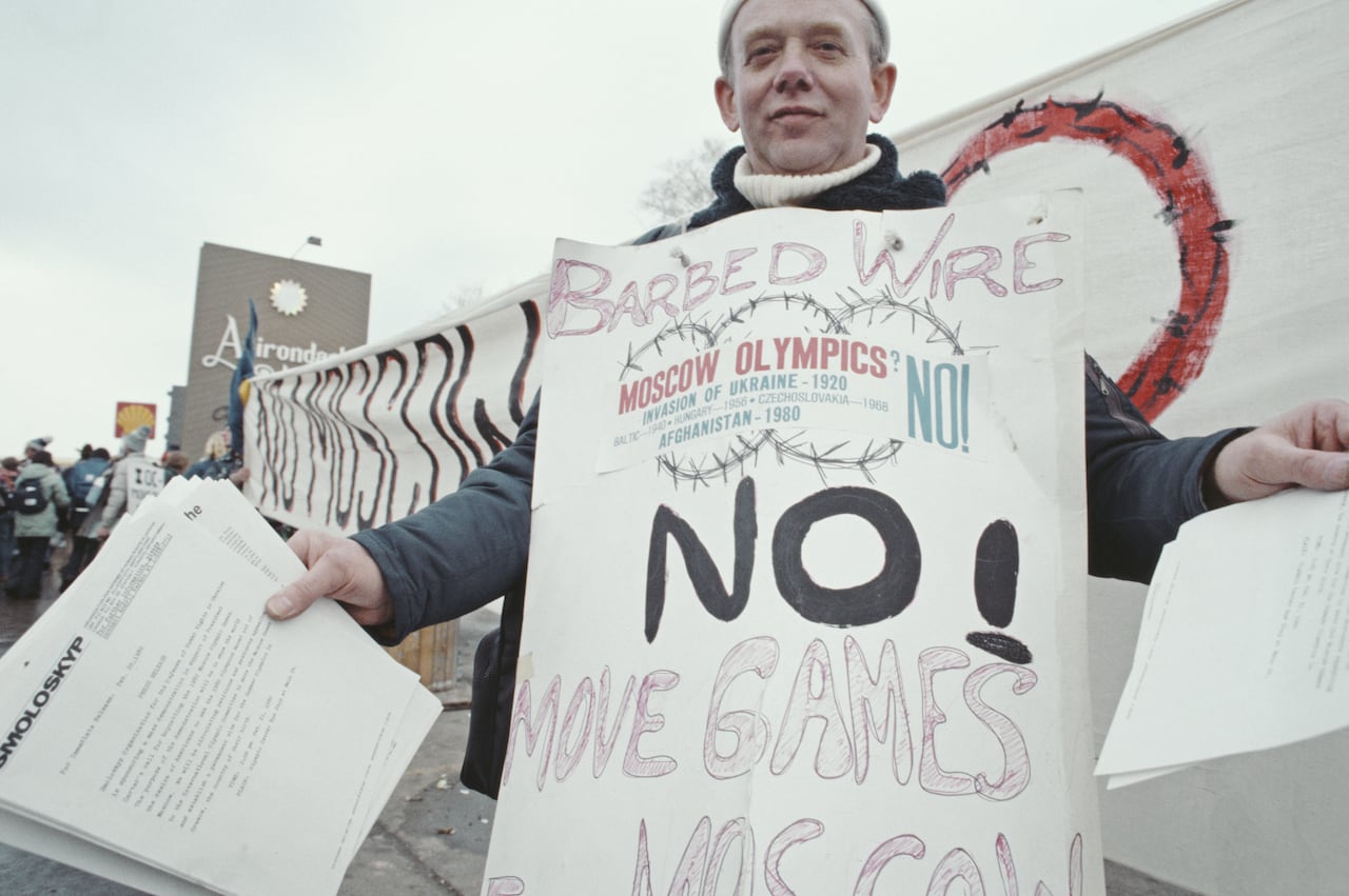 A protester wearing a placard and distributing leaflets against the Soviet Union invasion of Afghanistan and advocating for the boycott of the 1980 Moscow Summer Olympic Games during the Opening Ceremony for the XIII Olympic Winter Games