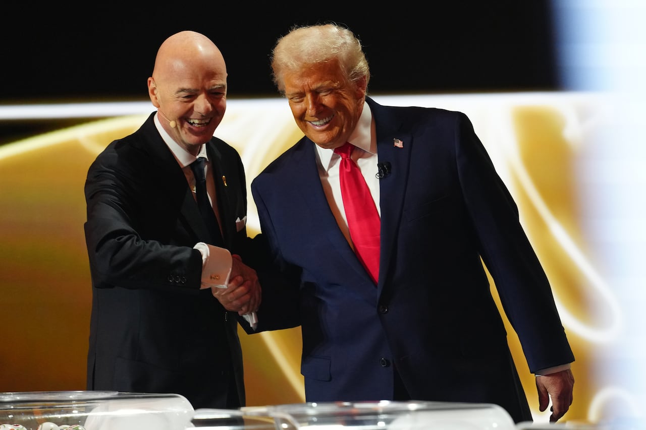 Two men in suits shake hands while smiling wide