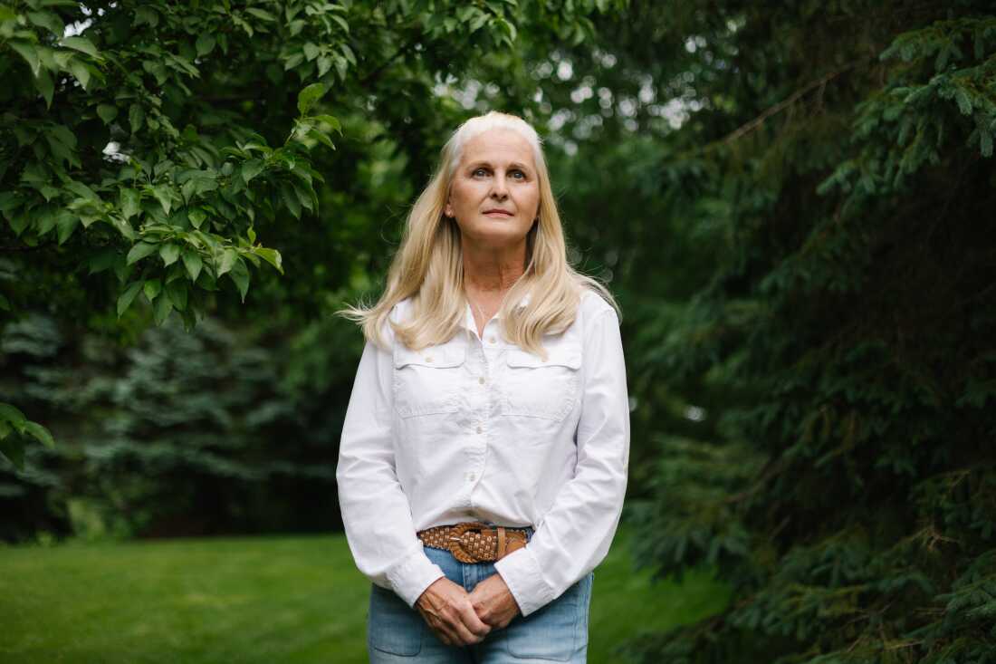 Rebecca Norton is shown standing alone outside with lush green trees around her.