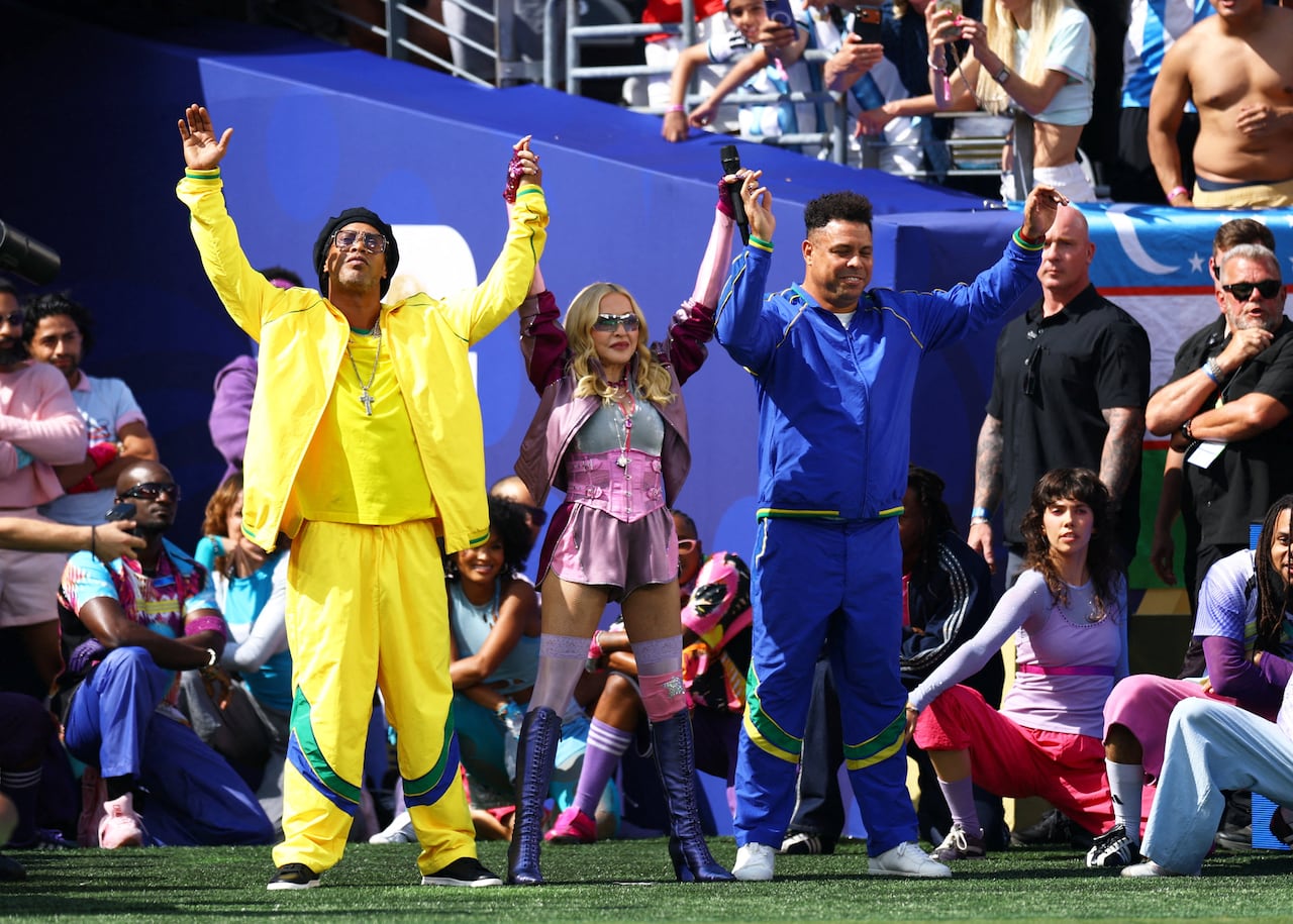 Three people stand in a stadium holding hands above their heads.