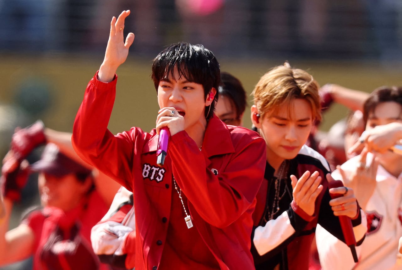 A man in a red jacket sings in front of dancers.