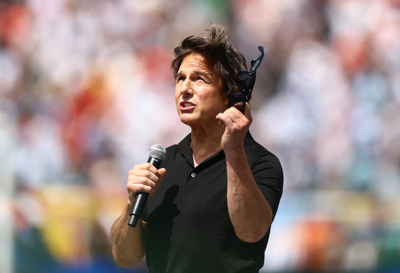 A man speaks into a microphone while holding sunglasses