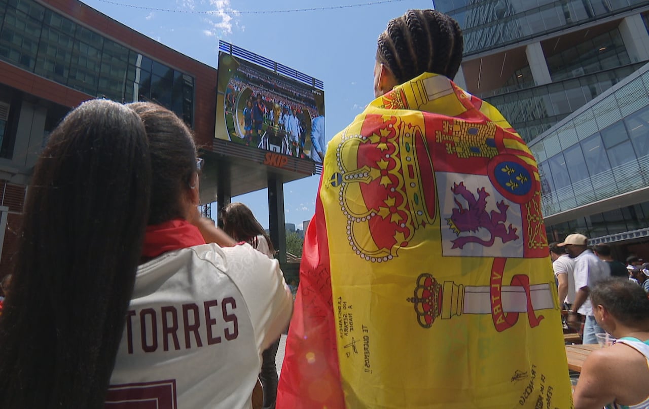 Two soccer fans, seen from behind, watching the World Cup on a big screen outside.