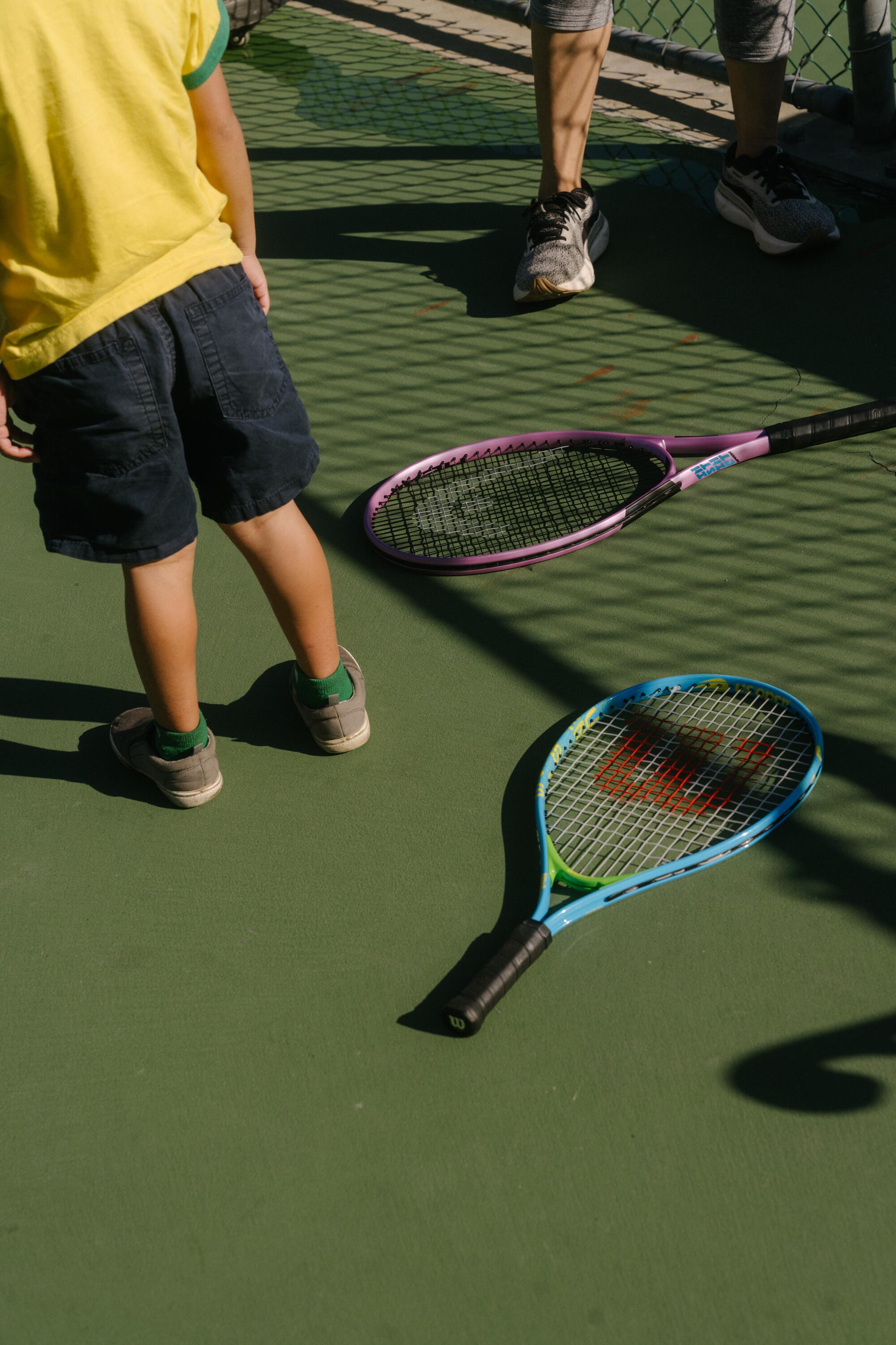 An adult tennis racket and a child's racket rest on the court.