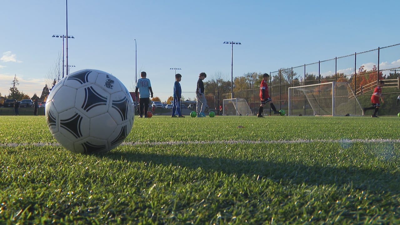 A soccer ball is pictured in the foreground with kids playing soccer in the background. 