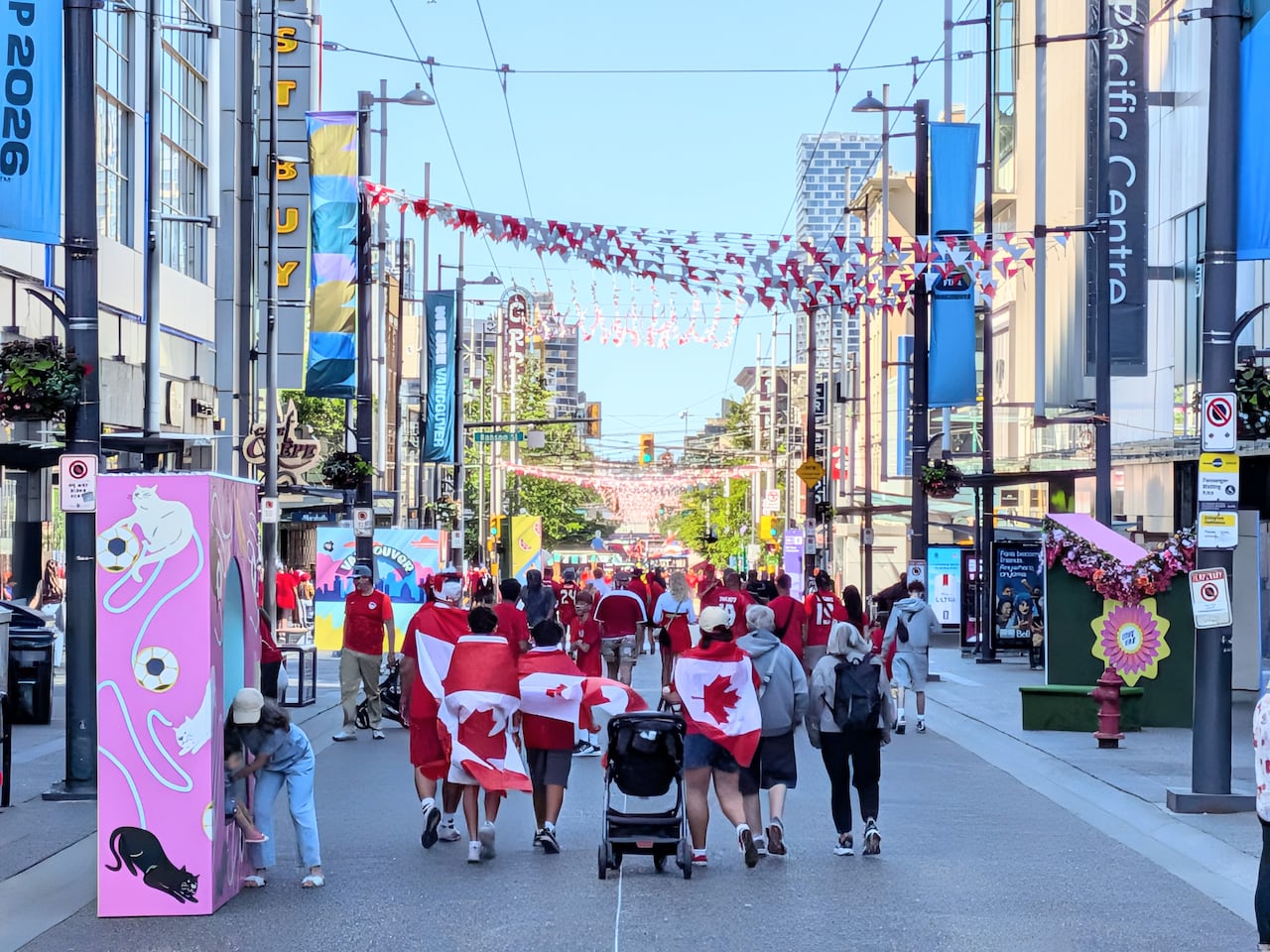 People in red shirts walk down a city street decorated in red and white.