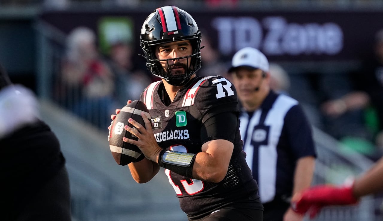 A football quarterback in black and red holds the ball as he looks on, ready to pass.