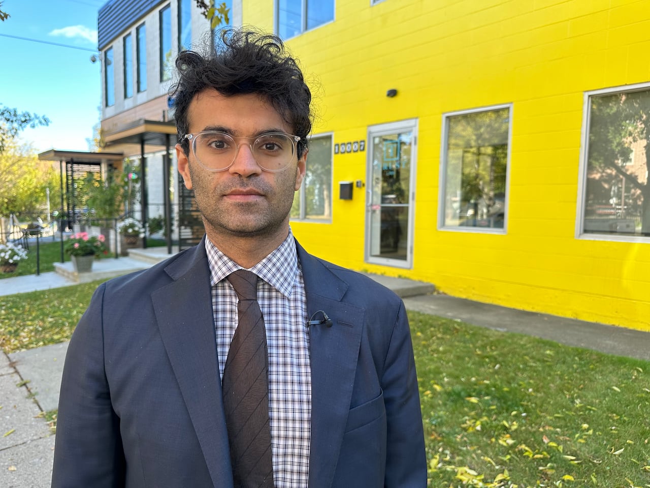 A man in a suit stands in front of a yellow building.