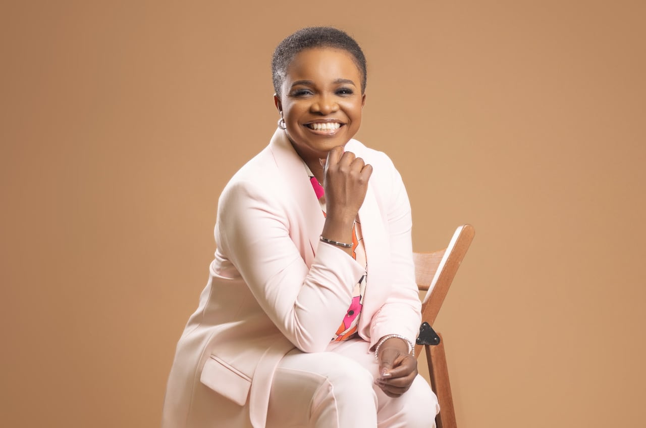 Woman poses and smiles in front of a light brown background.