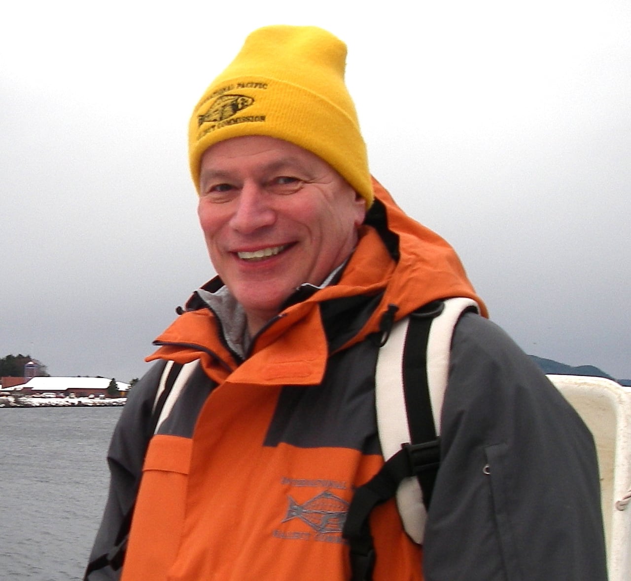 A man in a yellow hat and orange jacket with a white backpack on.