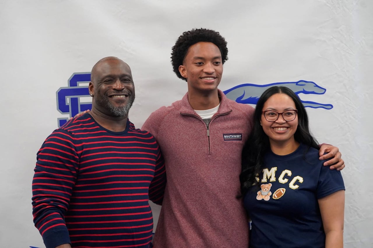 A young man stands in between a man and a woman as they pose for a photo.