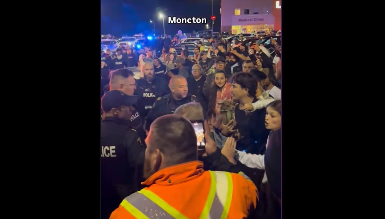 A screenshot of a video showing a large crowd in a parking lot, including police trying to manage it