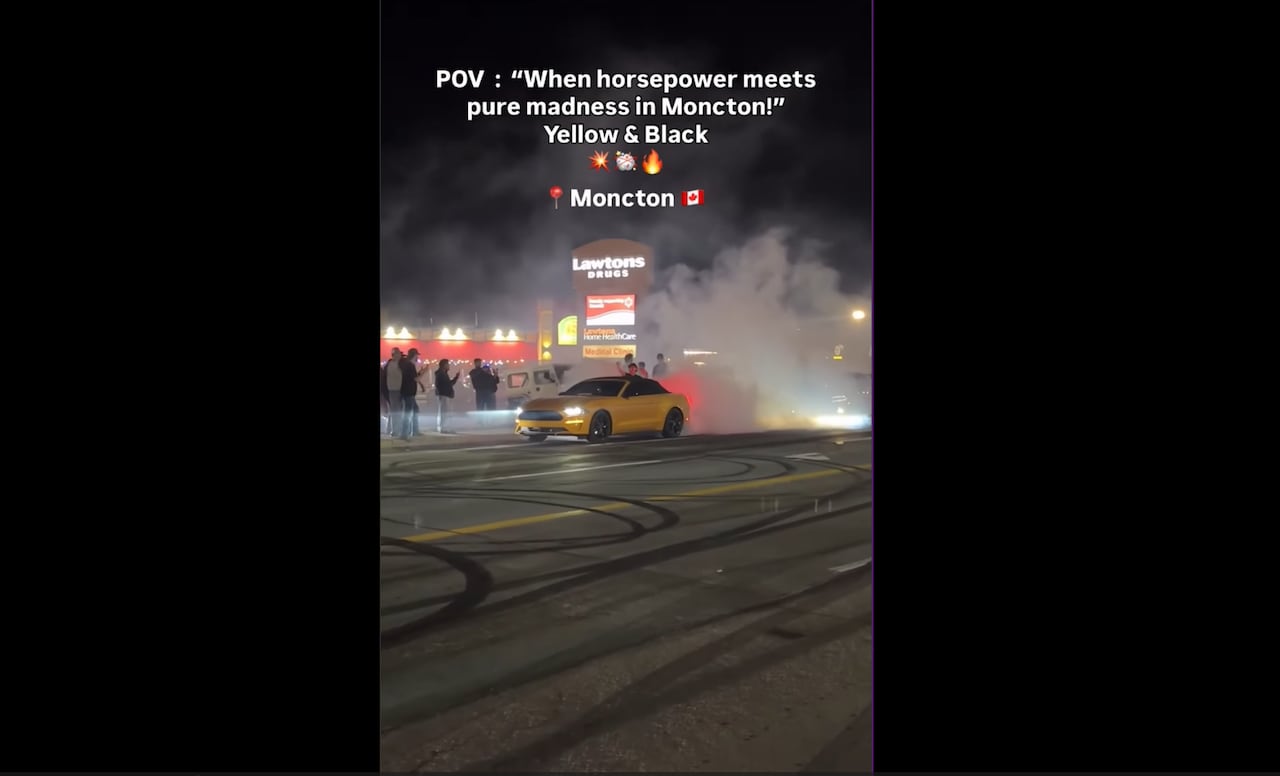 A yellow car doing burnouts in the street with black marks all over the street.