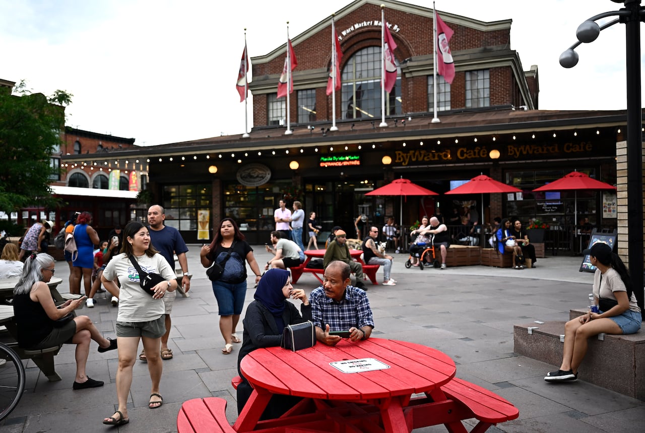 People sit at benches and tables and wander through a downtown plaza.