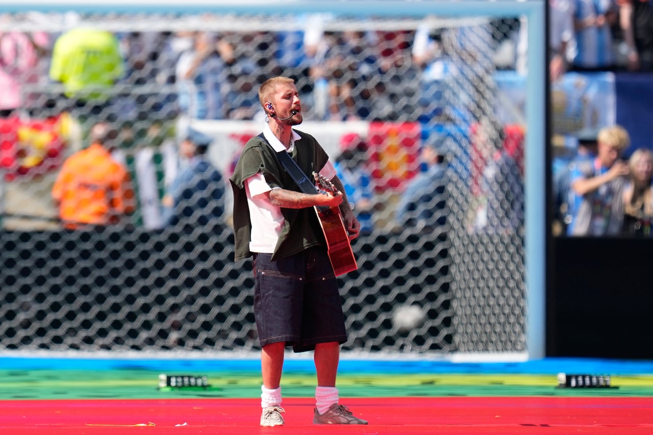 Justin Bieber plays a guitar while singing on the soccer pitch in front of a white net