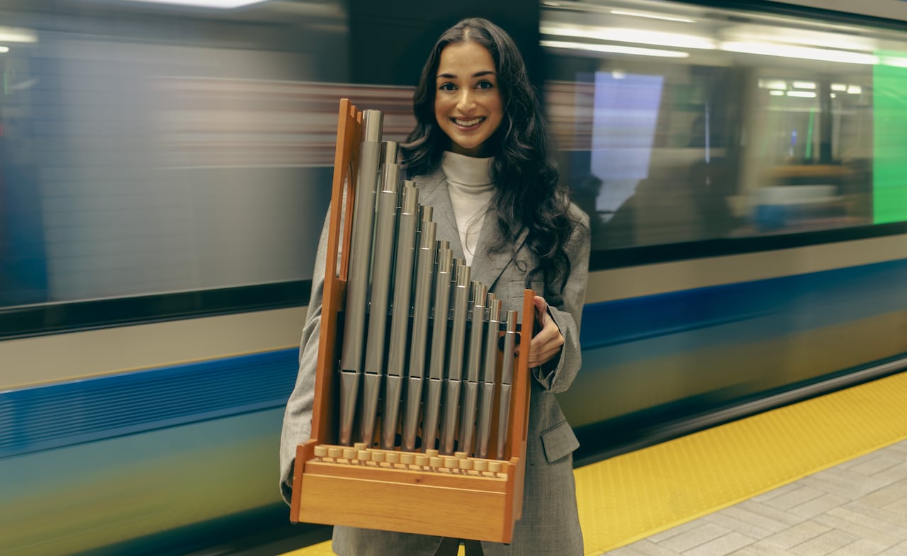Maria Gajraj holds a set of chamber organ pipes while a train whizzes behind her in the Montreal métro.