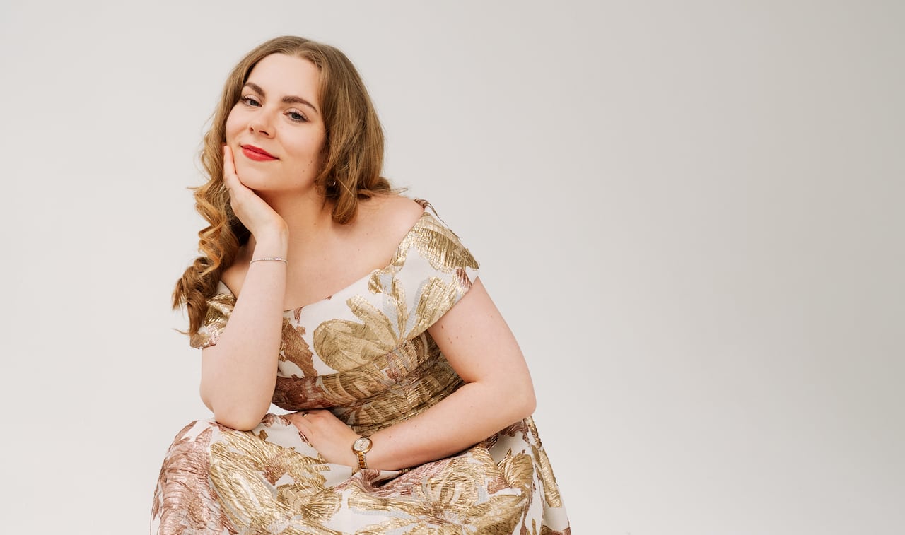 Emily Rocha sits on a stoot, wearing a floral dress.