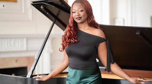 Wearing an off-the-shoulder black-and-green gown, soprano Nikan Ingabire Kanata leans against a grand piano.