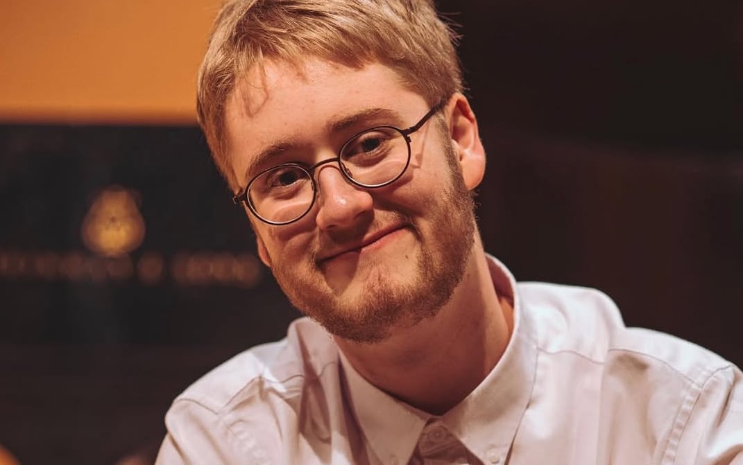 Wearing a white shirt, a smiling Grégoire Abadie looks at the camera with a grand piano in the background.