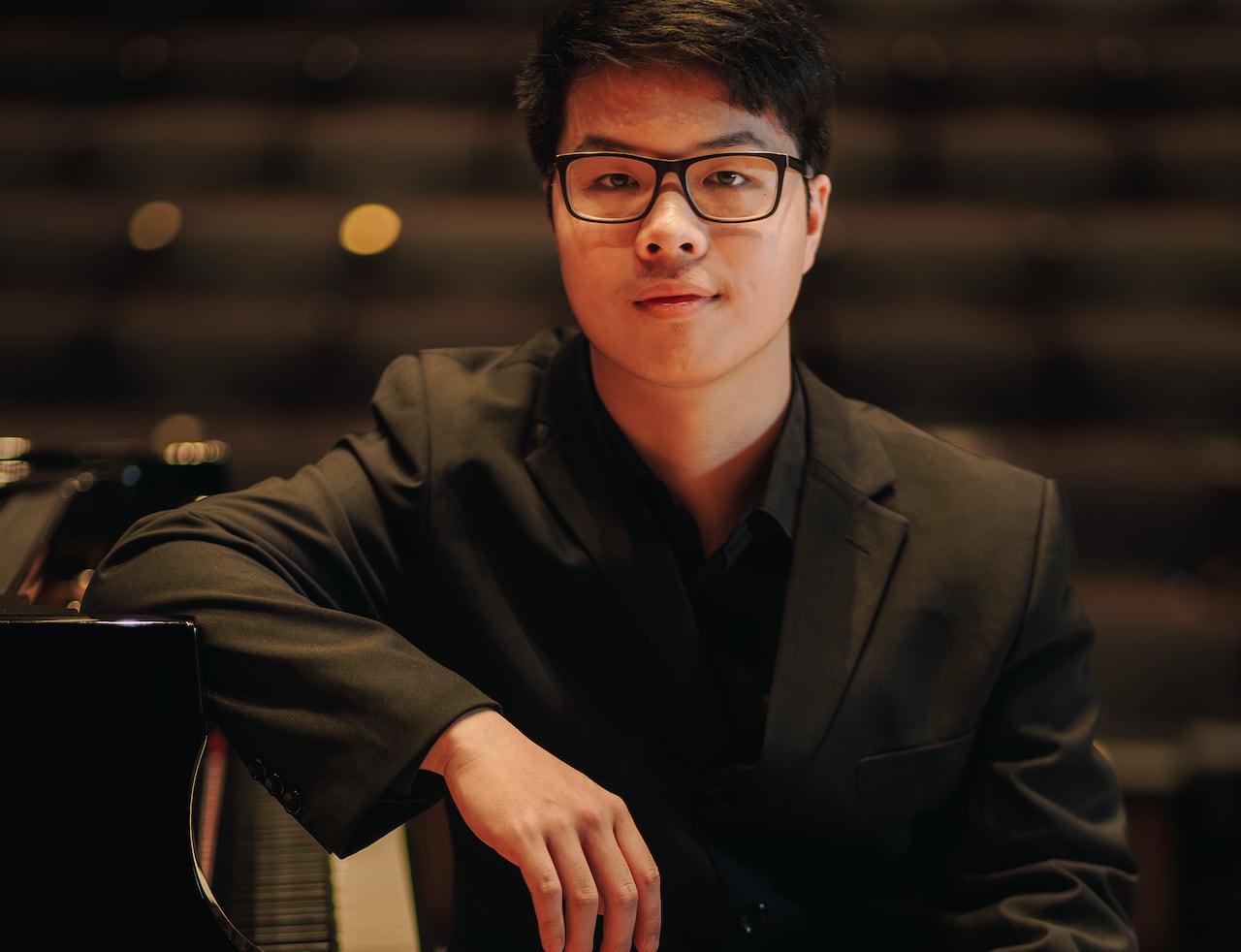 Dressed entirely in black, Brian Sun sits at the keyboard of a grand piano, onstage in a dimly lit concert hall.