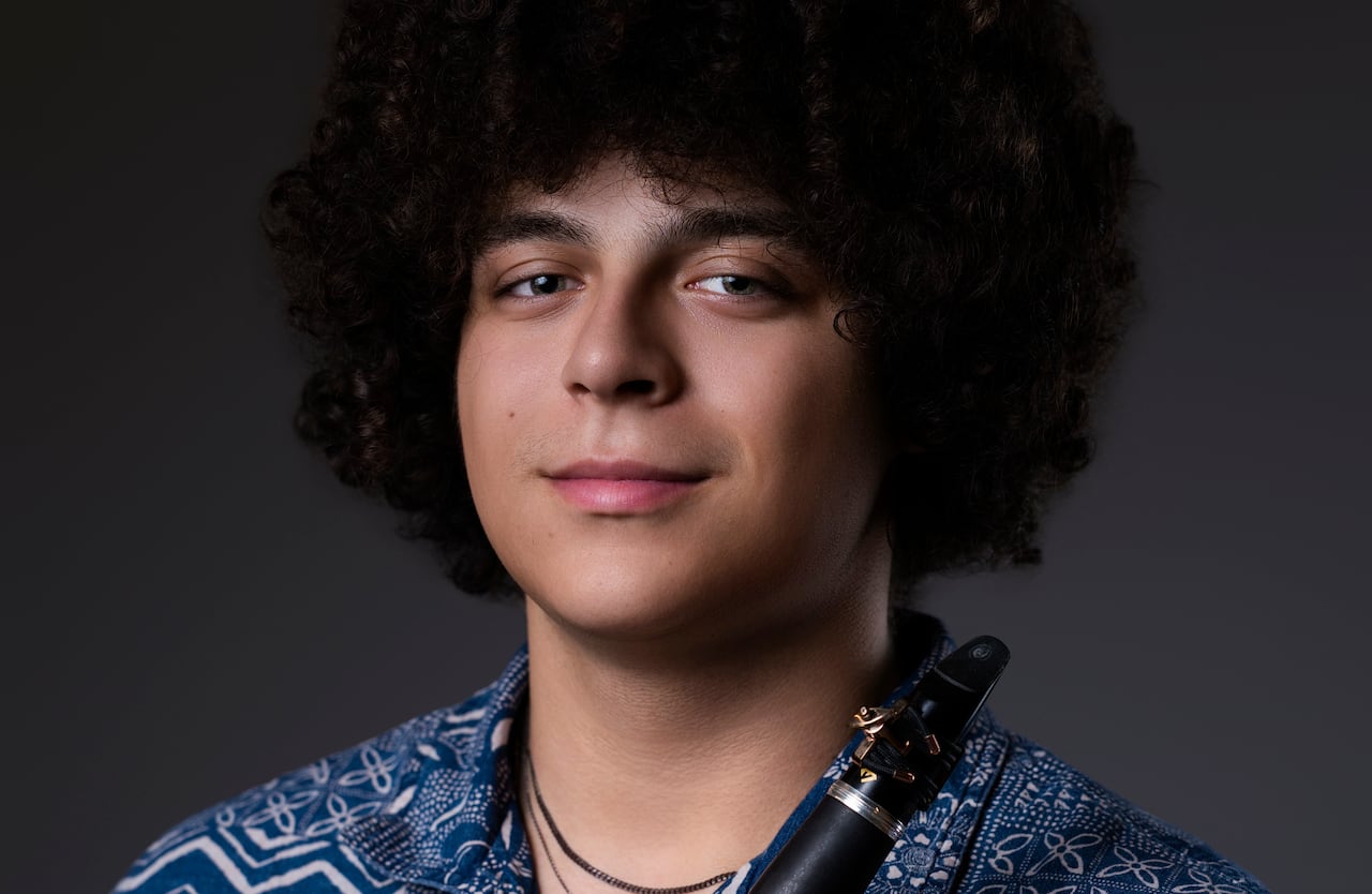 Wearing a blue patterned shirt, Kalvin Rowe looks into the camera while holding his clarinet.