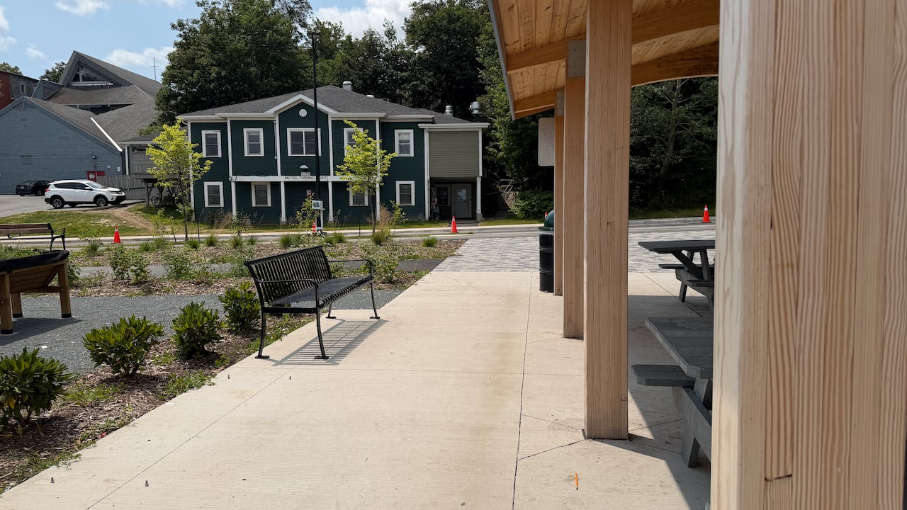 A park with a bench and shrubs. A green men's shelter is in the background.