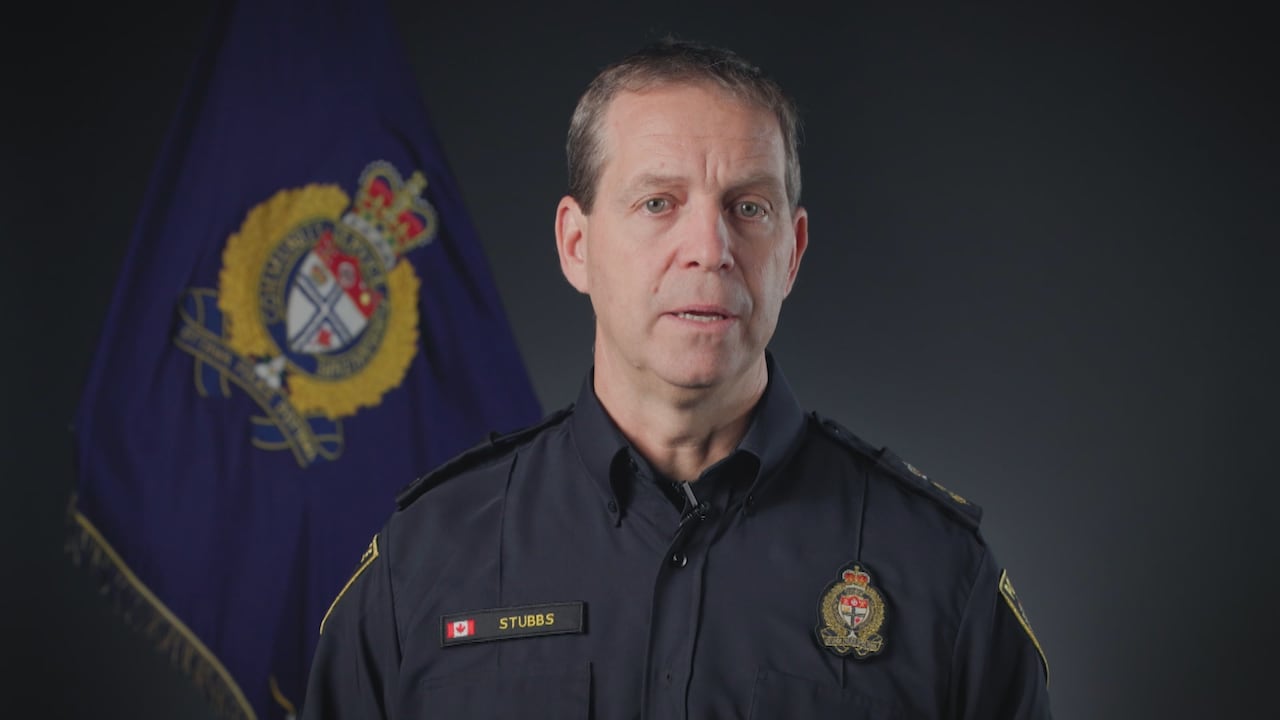 A man in a police uniform stands in front of a flag.