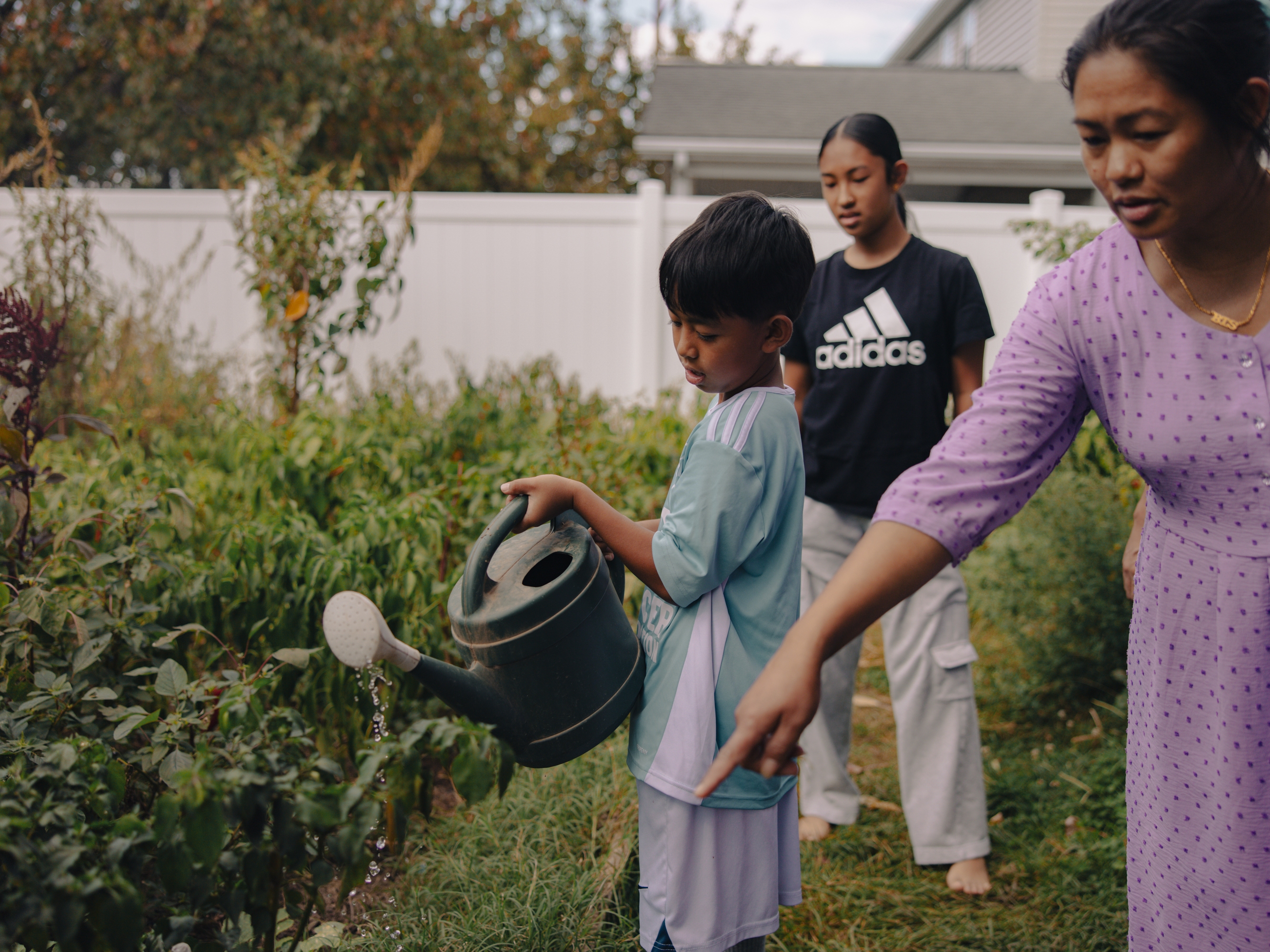 Aaron Tamang, 9, waters his family's backyard garden under the guidance of his mom, Nir Tamang, in Harrisburg, Pa., on Sept. 14, 2025. His sister, Naishi Tamang, 13, tags along.