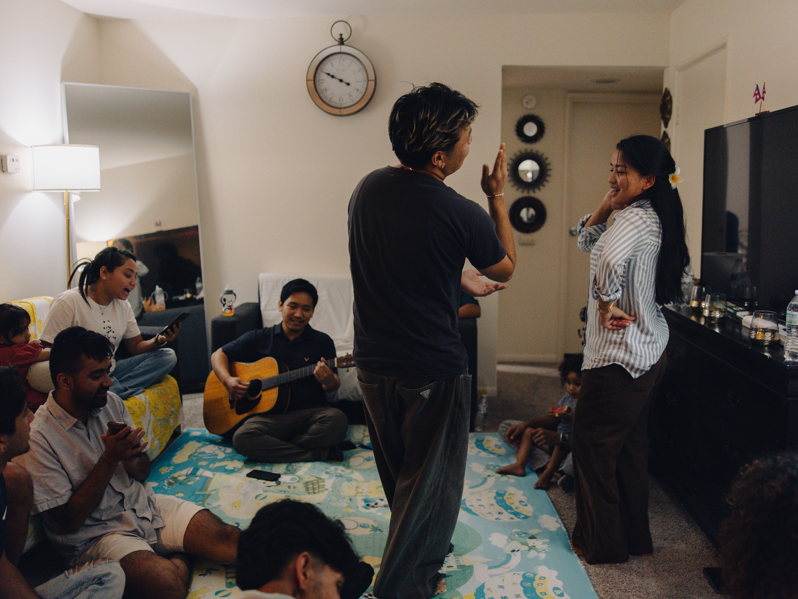 Community members gather for dinner and music at Robin Gurung's home in Harrisburg, Pa., on Sept. 14, 2025. Longtime friends Nawal Rai, who works as a storytelling and communications coordinator for ARU and runs the We Belong Here campaign, and Manju Gurung dance together as everyone sings together and Bibek Rai plays guitar.