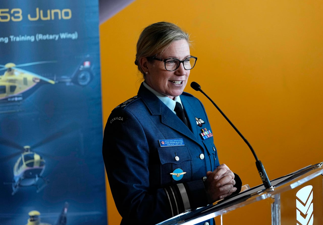 A woman in a military uniform stands in front of a banner depicting helicopters.