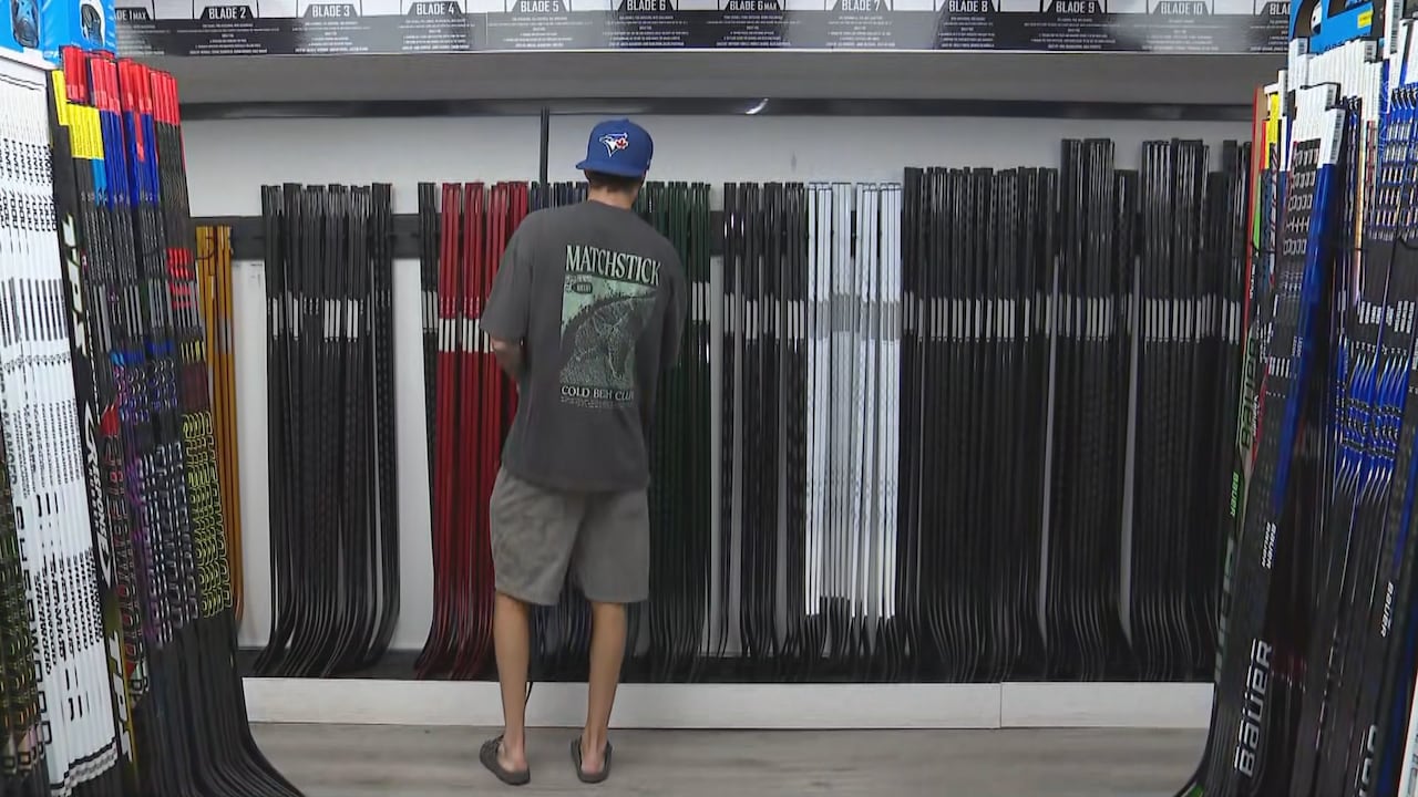 a man in shorts and a tshirt looks for a hockey stick on a rack full of them in a store