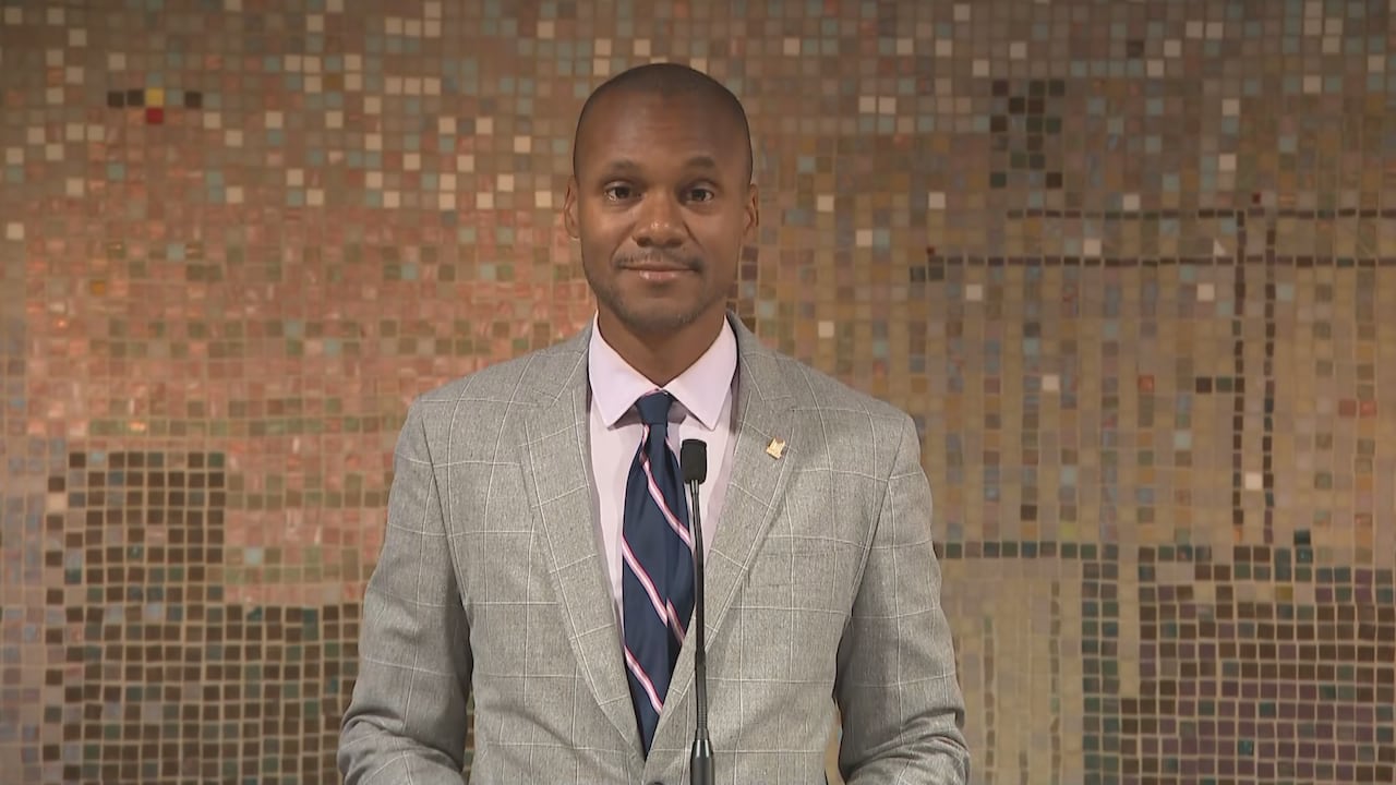 Man in suit and tie standing in front of microphone, looking at camera