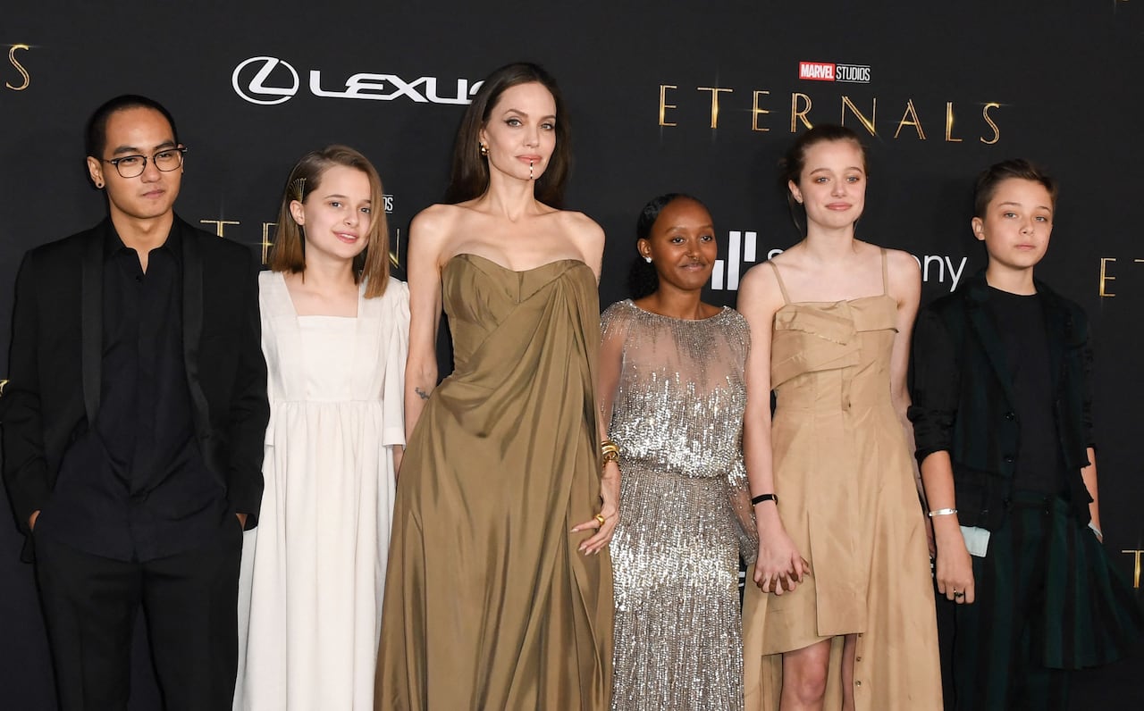 Women in brown dress stands in the centre, surrounded by five kids, who are also dressed up.
