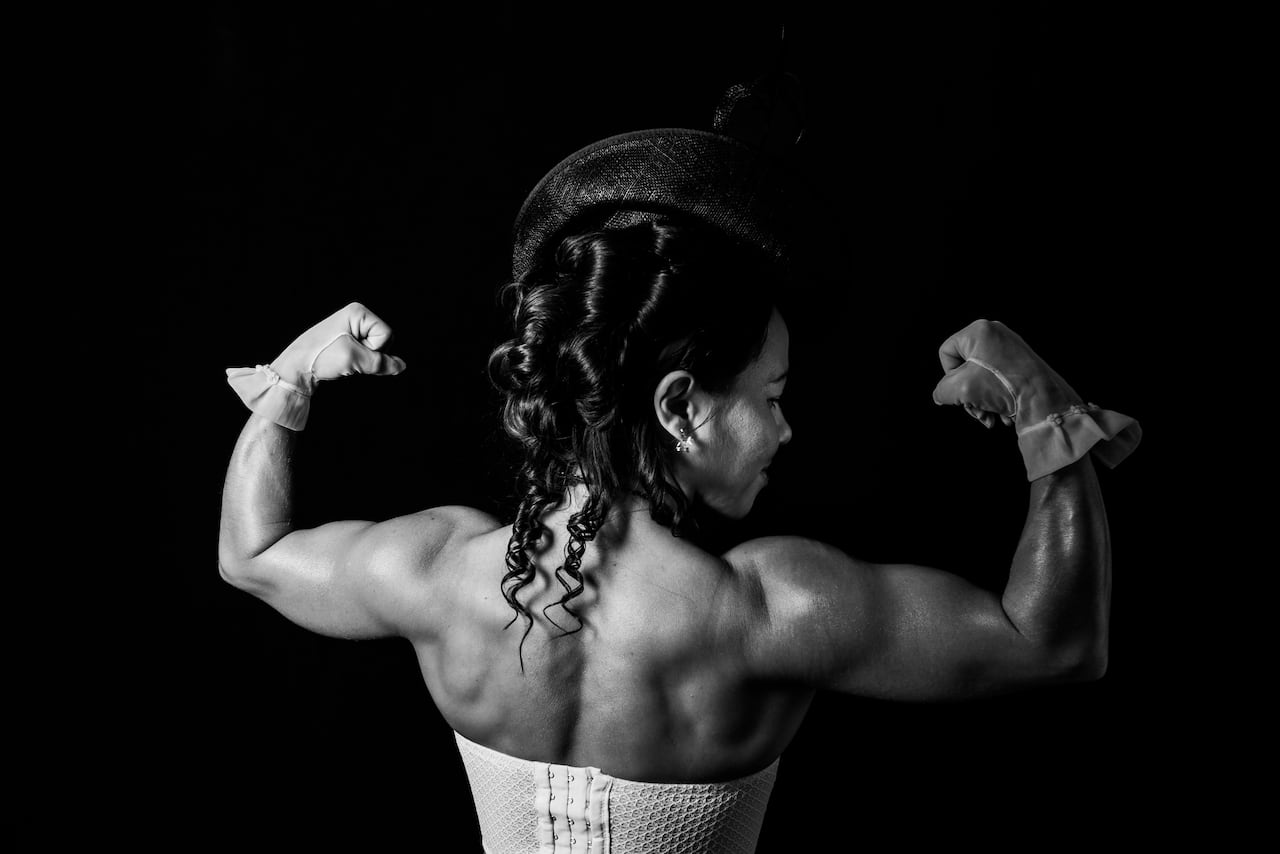 A black and white photo of a woman with long black hair flexing her arms.