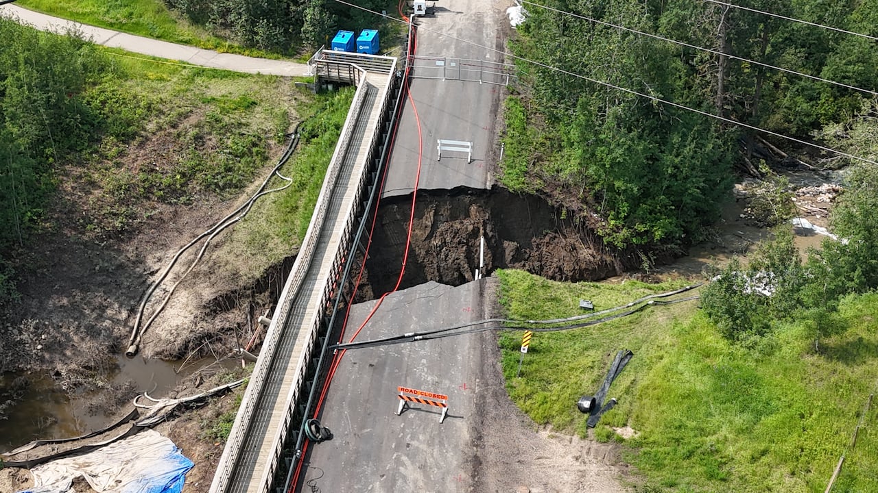Drone footage of a part of a road that collapsed by a creek.