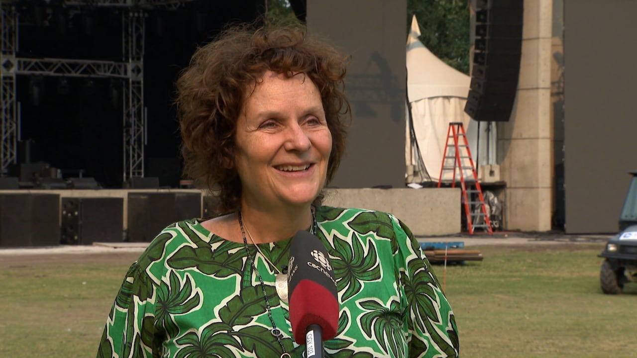 A woman wearing a green shirt stands in front of a microphone and smiles at a reporter off camera.