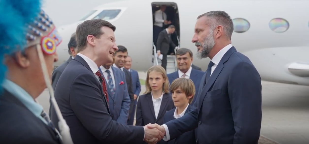 A group of people in suits stand before a plane.