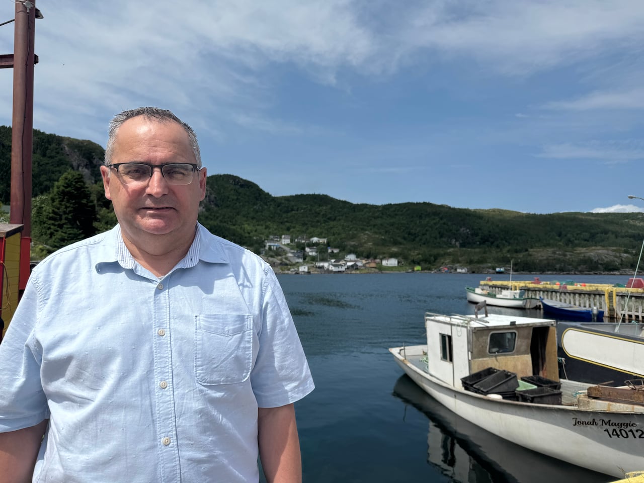 A man standing outside on a wharf, along a small harbour.