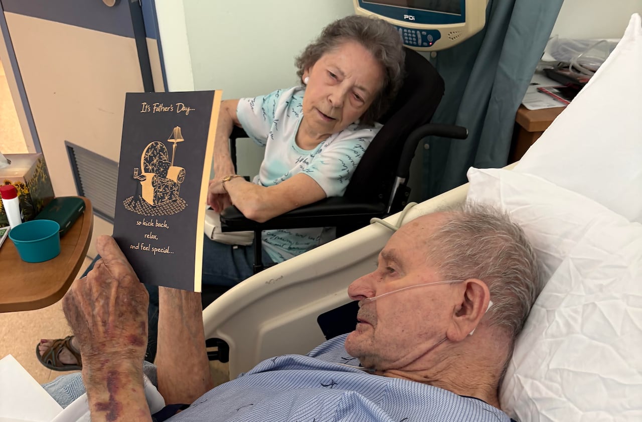 A man reading to his wife from a hospital bed.
