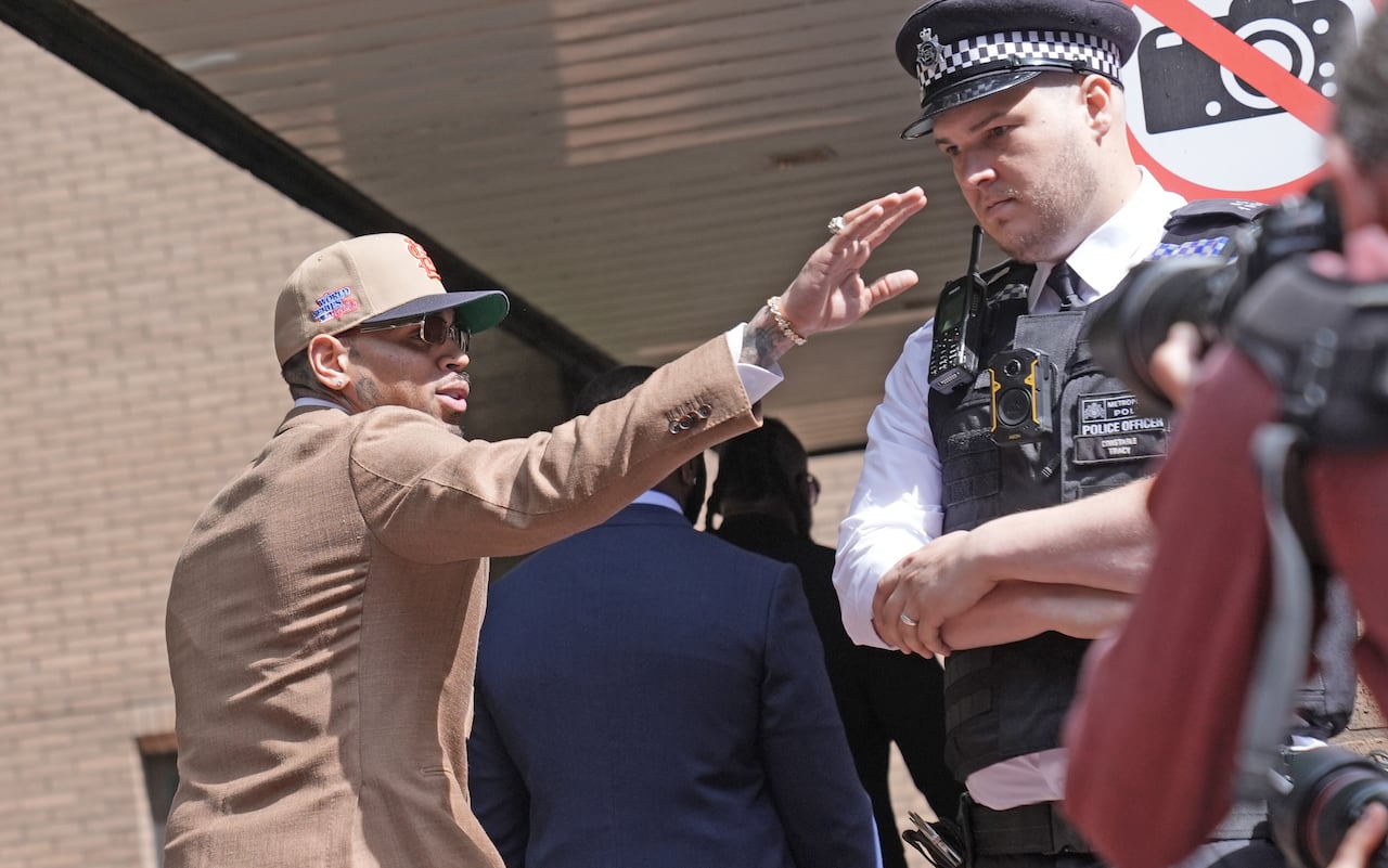 A man waves to people off camera, while walking past a police officer and into a building.