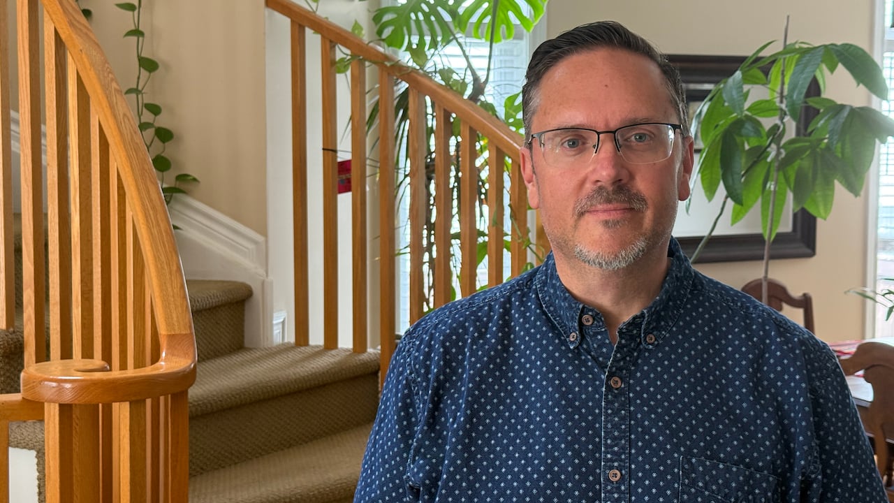 A man in front of a residential stair case with a plant behind him