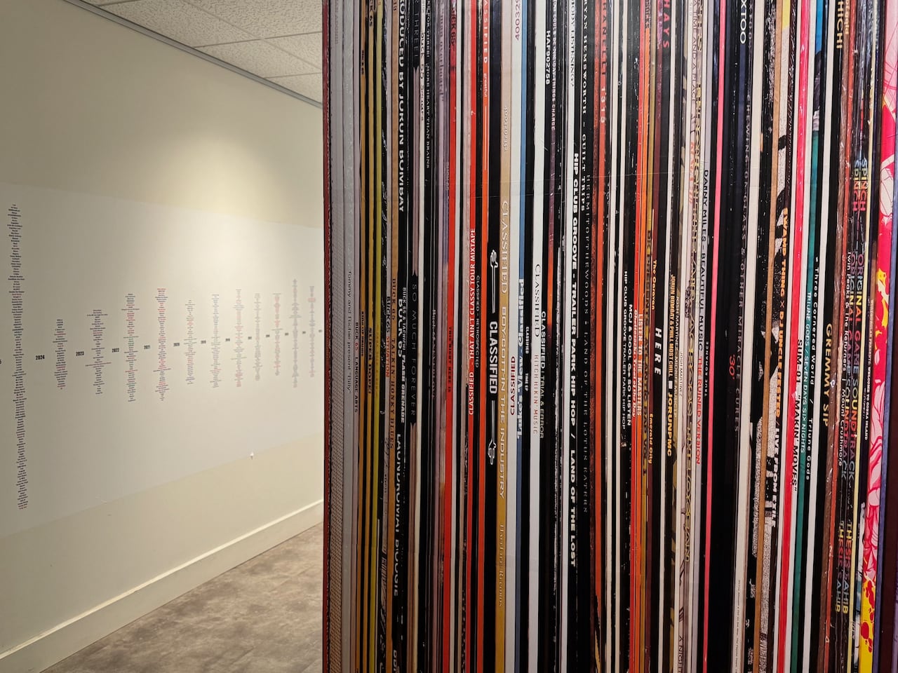 A brightly lit archive room with rows of tall metal shelving packed tightly with vinyl records and CDs. Two bald men with full bear